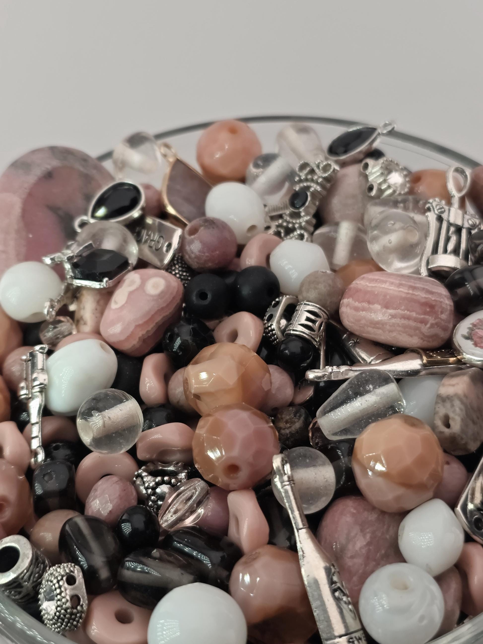 A close-up image of a collection of various beads, charms, and other decorative items arranged in a glass container.
