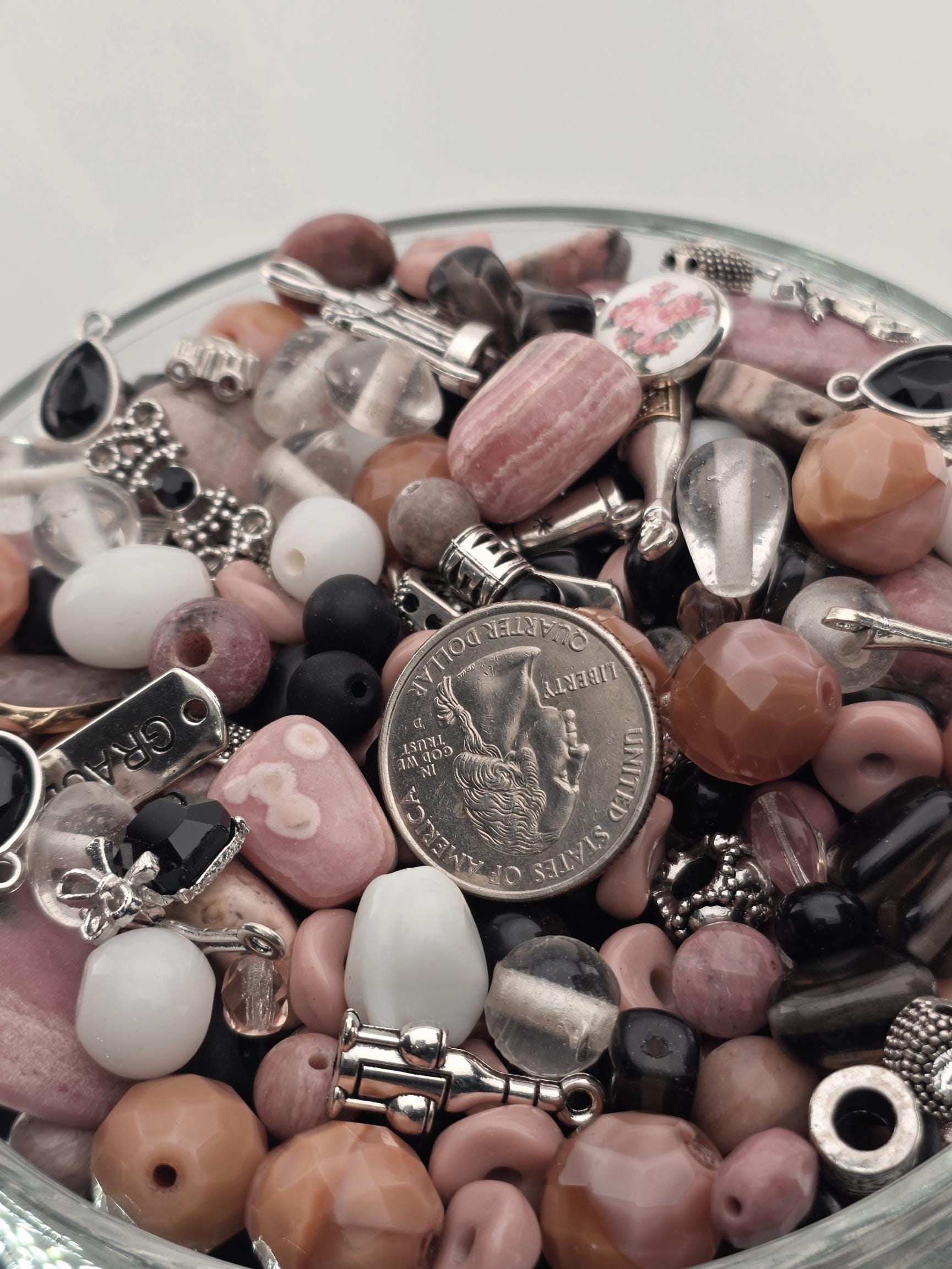 A close-up image of various beads, charms, and a coin, all arranged in a glass container.