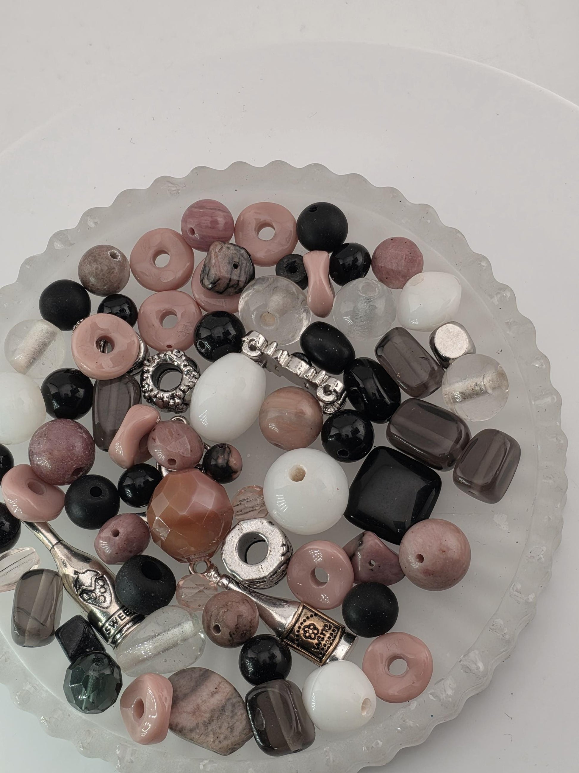 A glass bowl filled with various beads, including clear, black, and multicolored beads, as well as some metal beads.