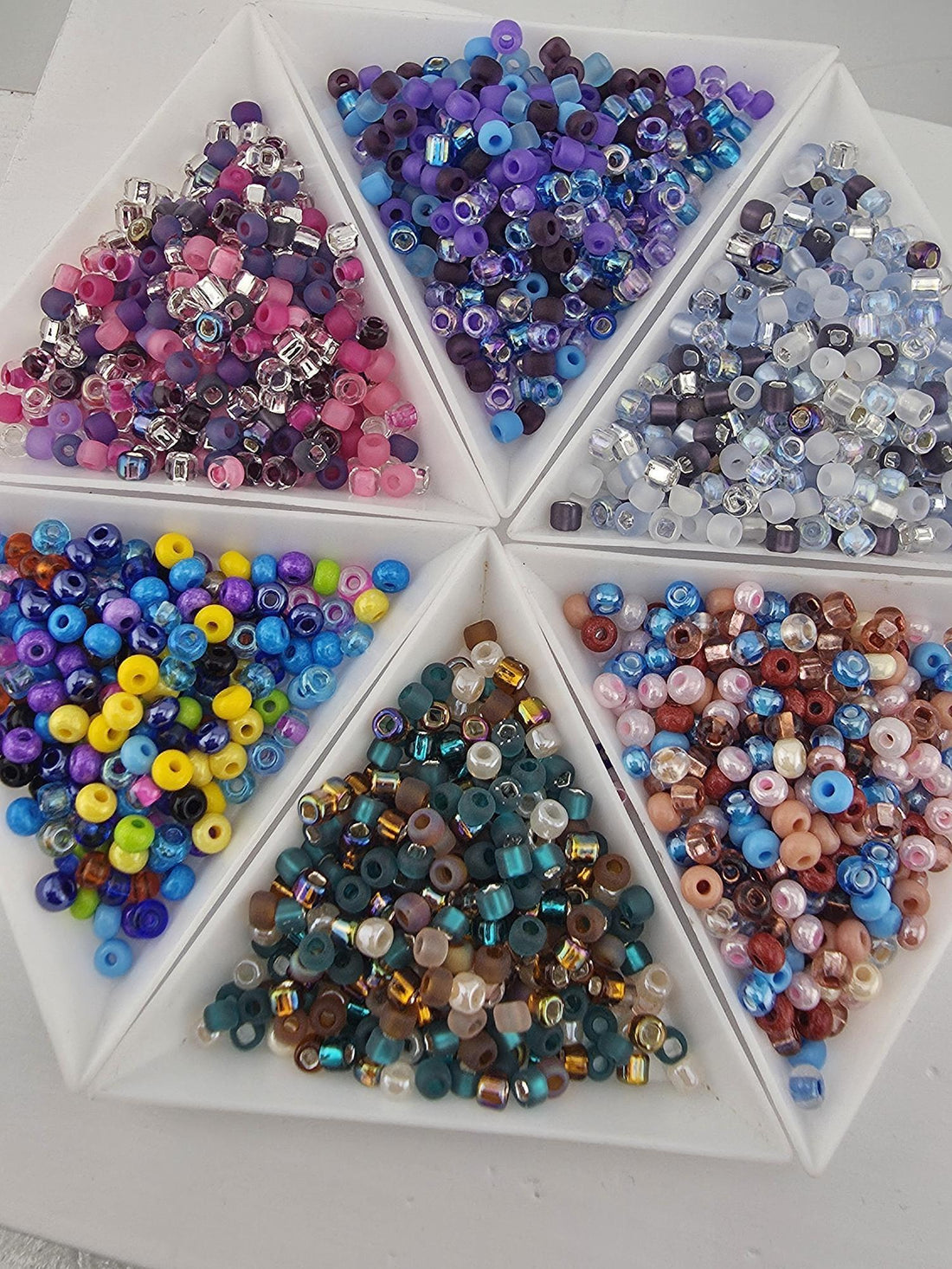 a collection of various colored seed beads in different shapes and sizes, arranged in multiple containers.