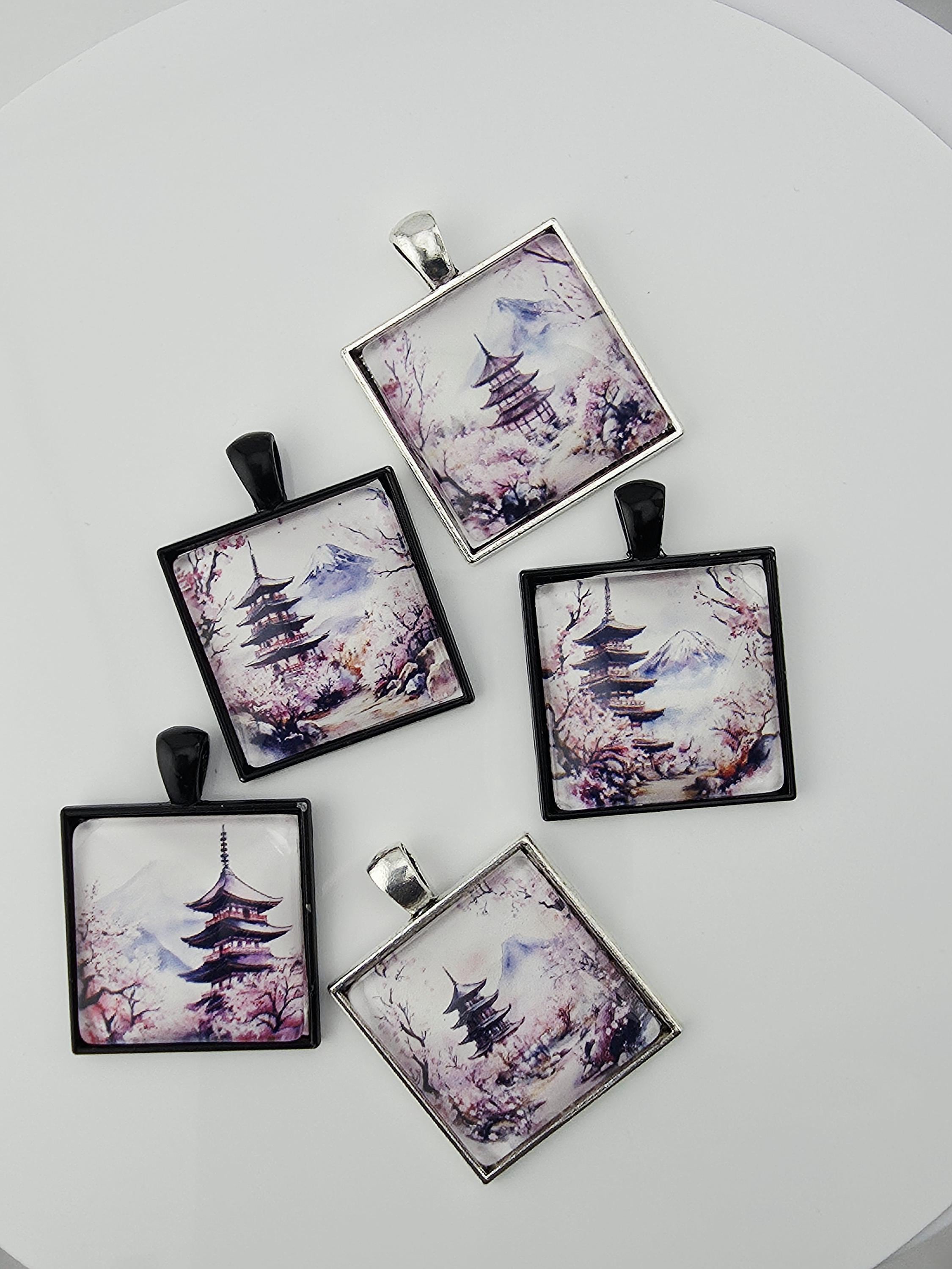 a collection of square pendants with various floral designs, including cherry blossoms and pagodas, arranged on a white surface.