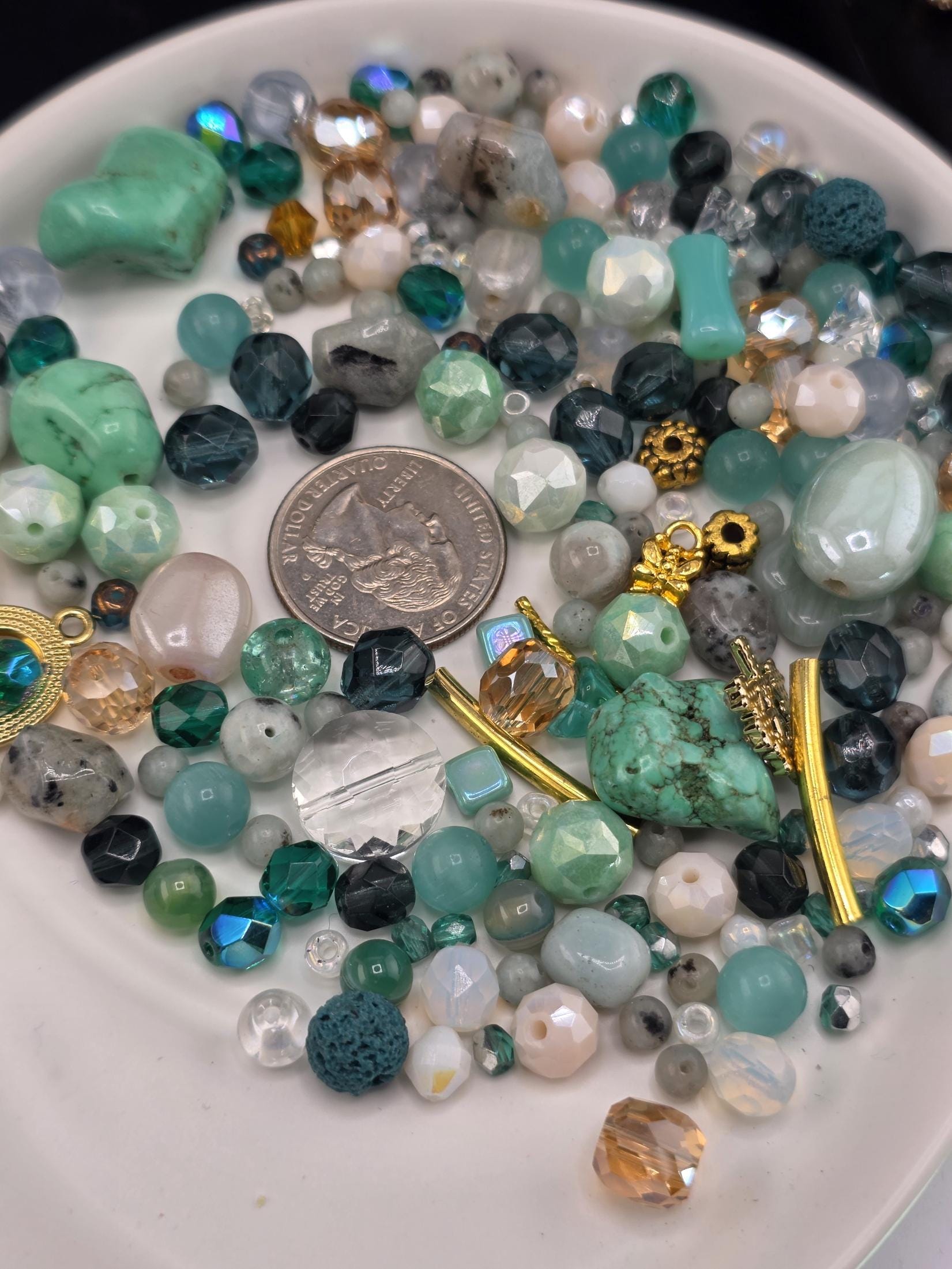 A collection of various beads, gemstones, and jewelry pieces, including a silver coin, arranged on a white plate.