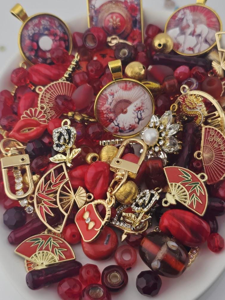 The image is a collection of various red and gold jewelry pieces, including pendants, charms, and beads, arranged on a white surface.