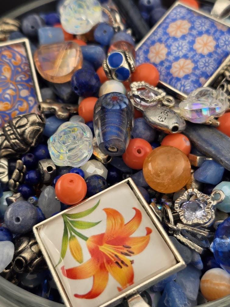 The image is a close-up of a collection of colorful beads, charms, and glass beads, including blue, orange, and silver elements, arranged in a visually appealing manner.