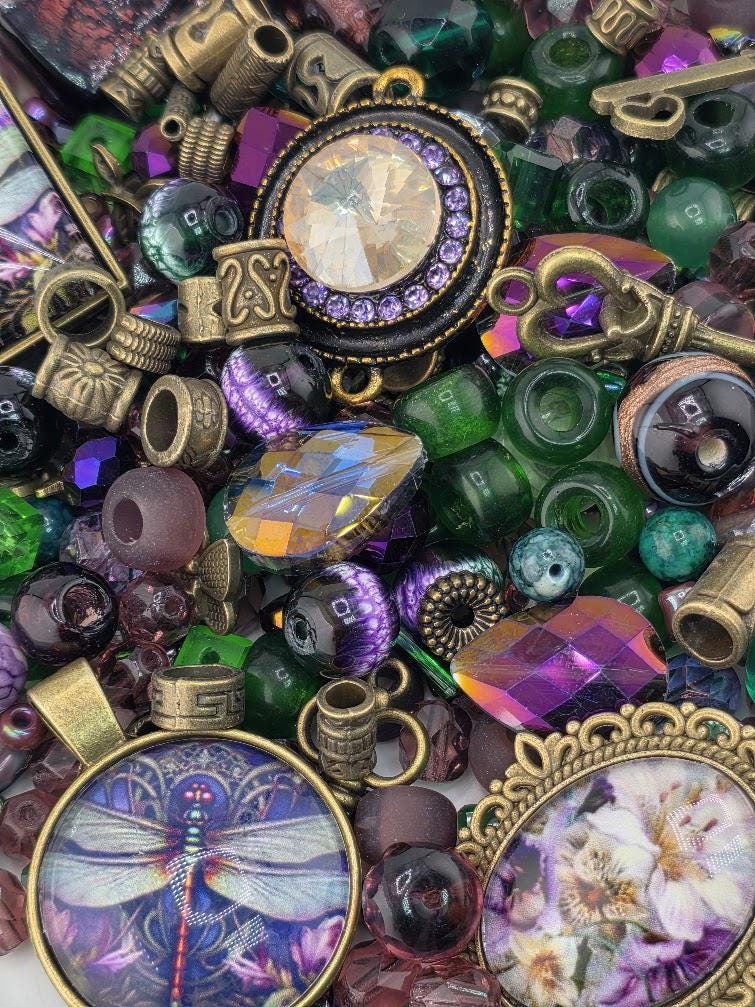 The image is a collage of various colorful beads, charms, and metallic objects, including a large gemstone, a dragonfly design, and floral elements.