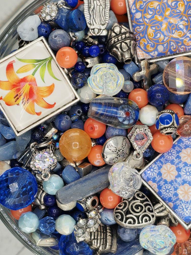 The image is a collection of various beads, charms, and other decorative items, including blue, orange, and silver elements, arranged in a visually appealing manner.