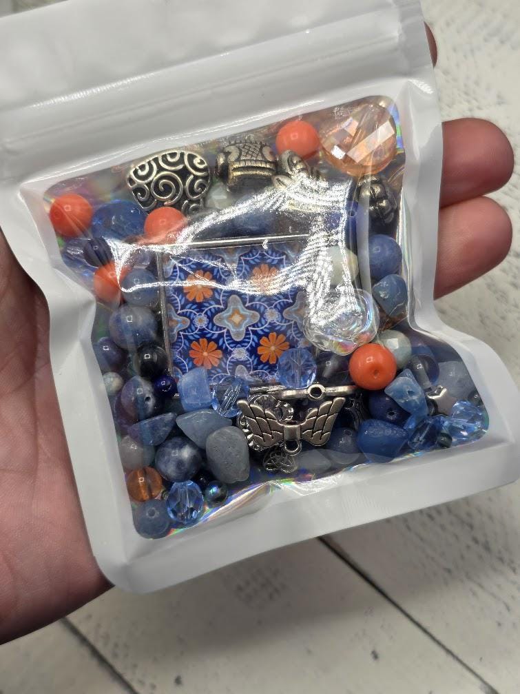 A hand is holding a small bag filled with various colorful beads, charms, and other small items.