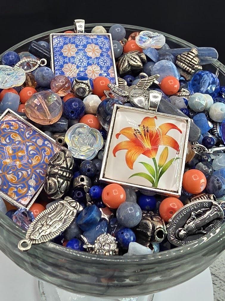 A glass bowl filled with various colorful beads, charms, and pendants, including a large orange flower-shaped charm.