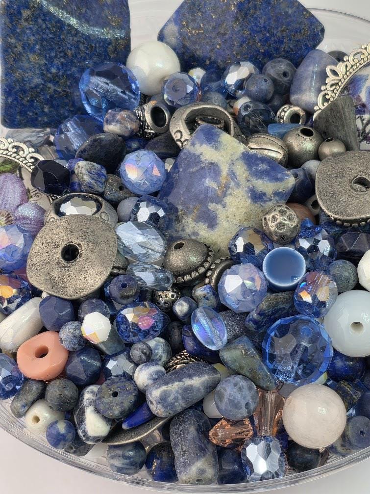 The image is a collection of various blue and silver beads, charms, and stones, including crystals and gemstones, arranged in a visually appealing manner.