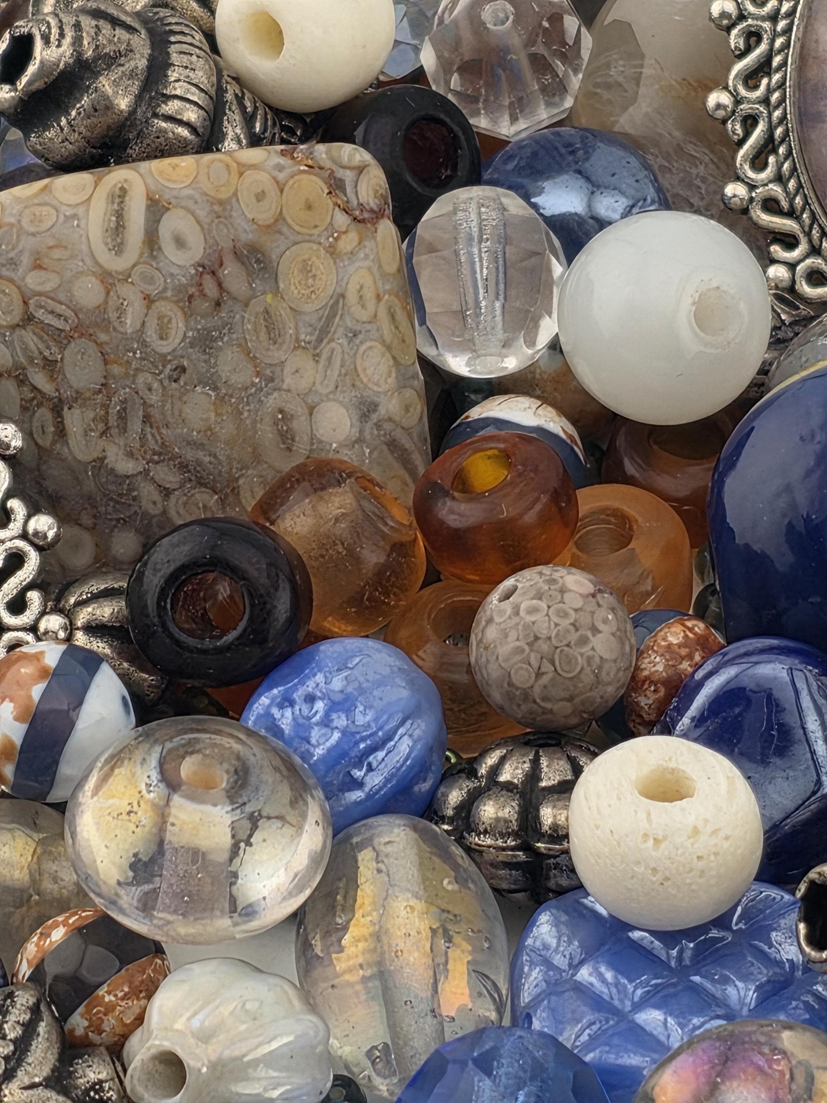 The image is a close-up of various beads and glass objects, including clear, white, and multicolored glass beads, as well as some metal and stone beads.