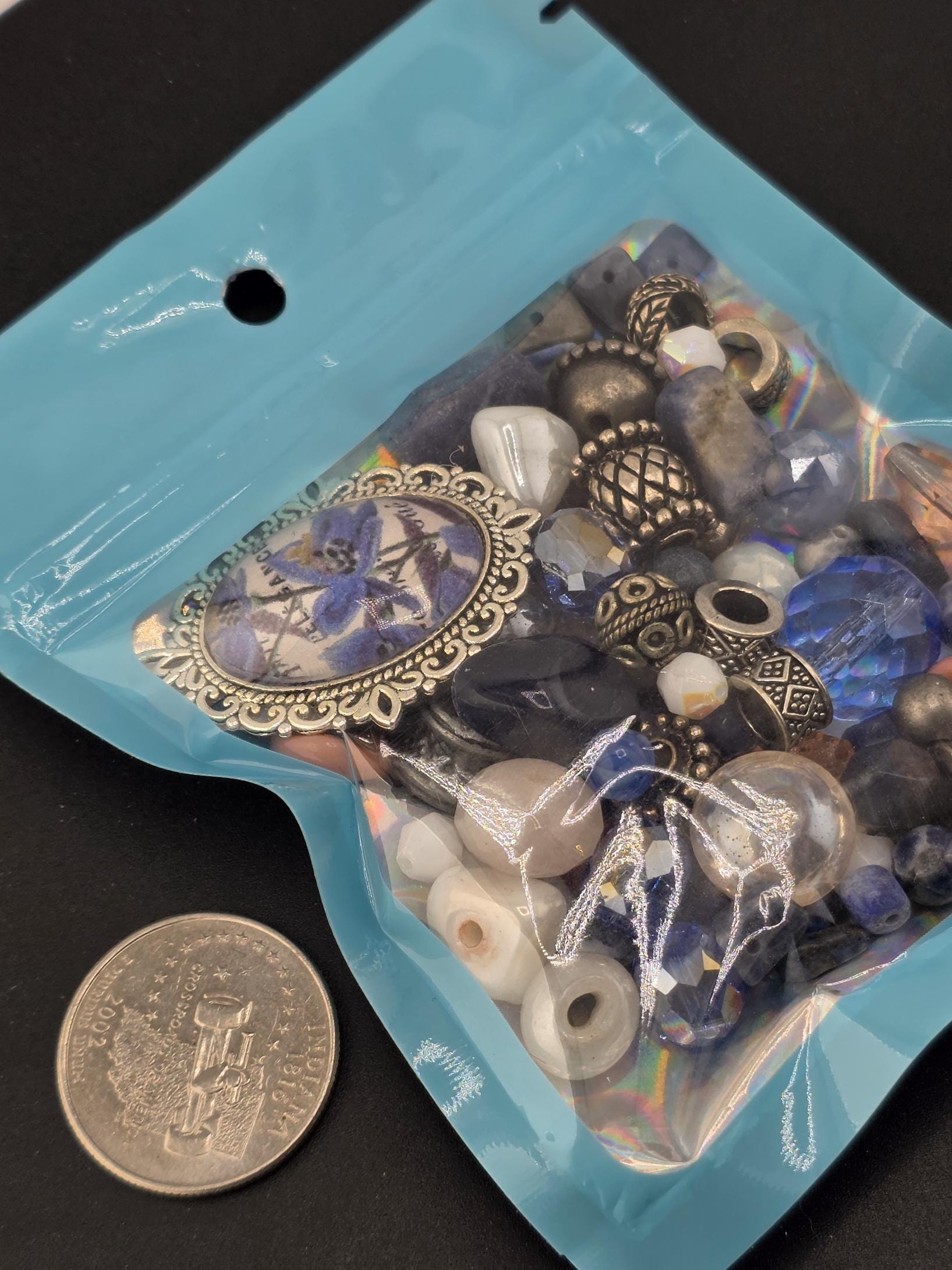 A blue bag filled with various beads and a silver coin are placed on a black surface.