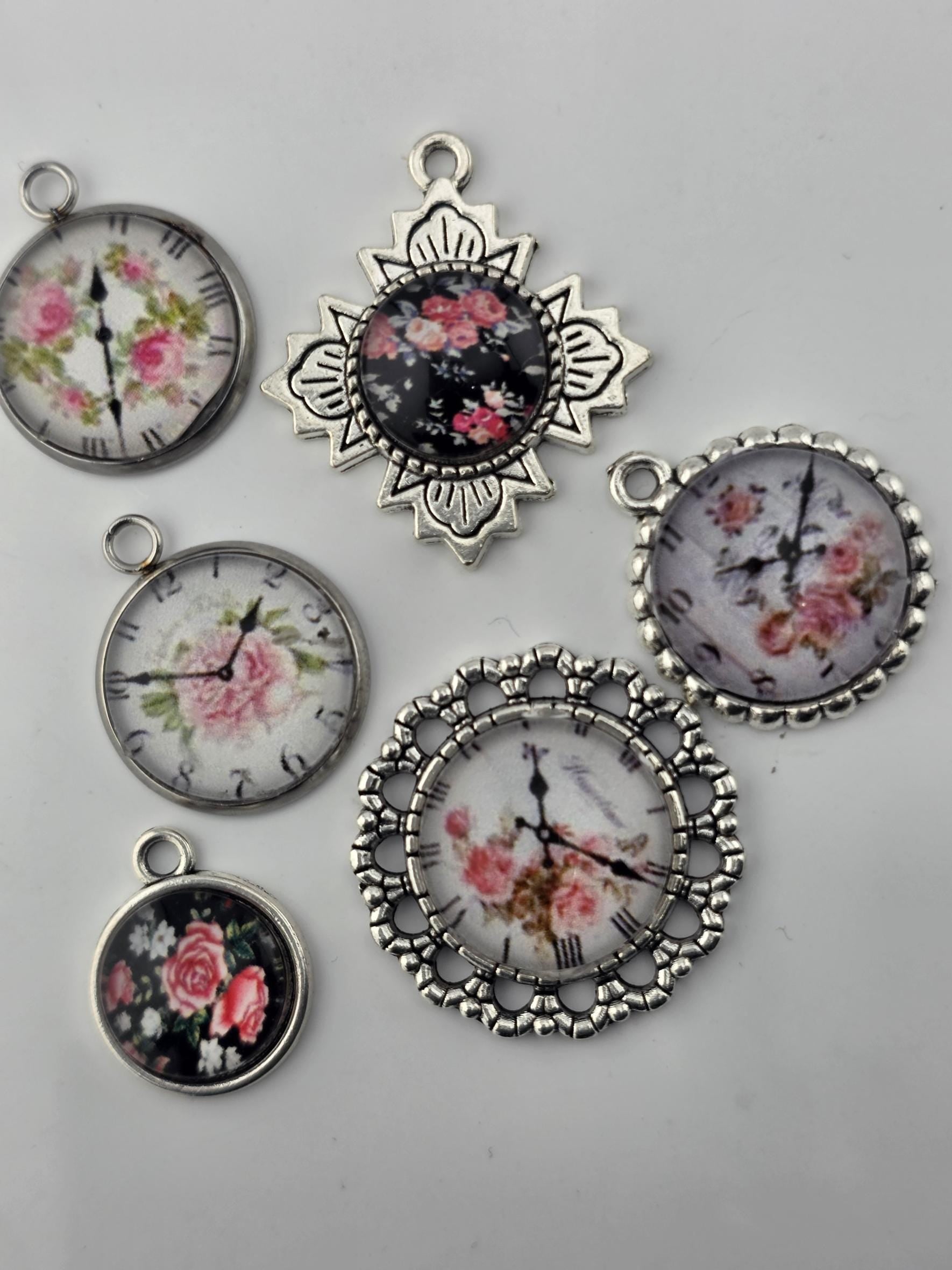 five pendants or charms, each featuring a floral design on the face of a clock. The pendants are arranged on a white surface, showcasing their intricate and decorative details.