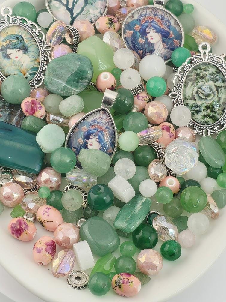 The image is a collection of various beads, charms, and pendants, including green, pink, and white beads, as well as some with floral designs. The objects are arranged in a visually appealing manner, creating a colorful and diverse display.