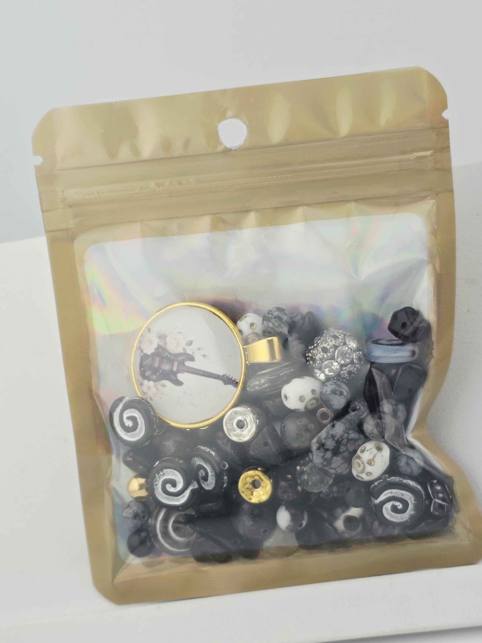 A clear plastic bag containing various beads and charms, including a pendant with a guitar design.