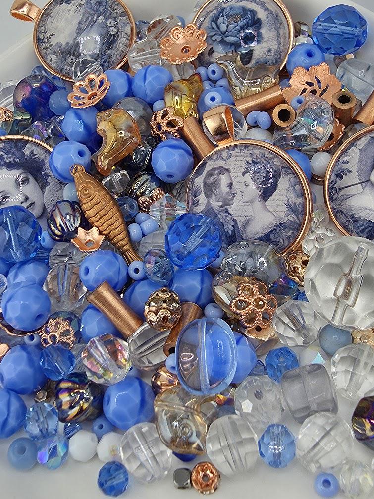 The image is a collection of various beads, charms, and trinkets in shades of blue, gold, and clear, scattered together.