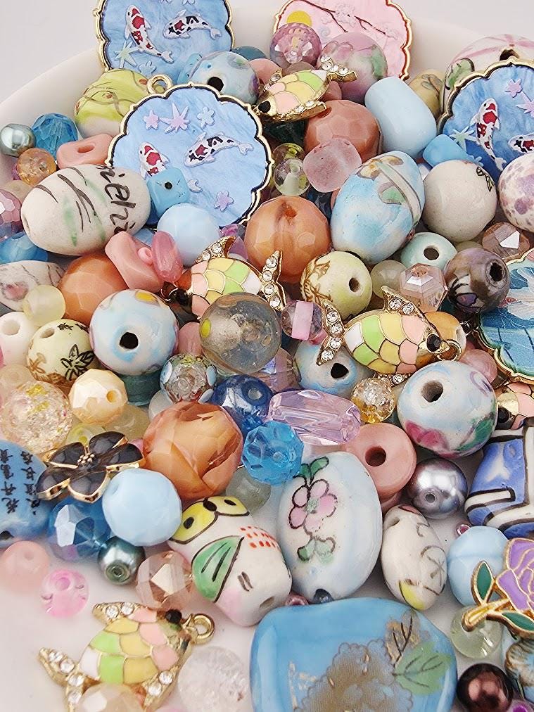 The image is a colorful assortment of various beads, charms, and trinkets, including multicolored glass beads, metal beads, and other decorative elements, all arranged on a surface.