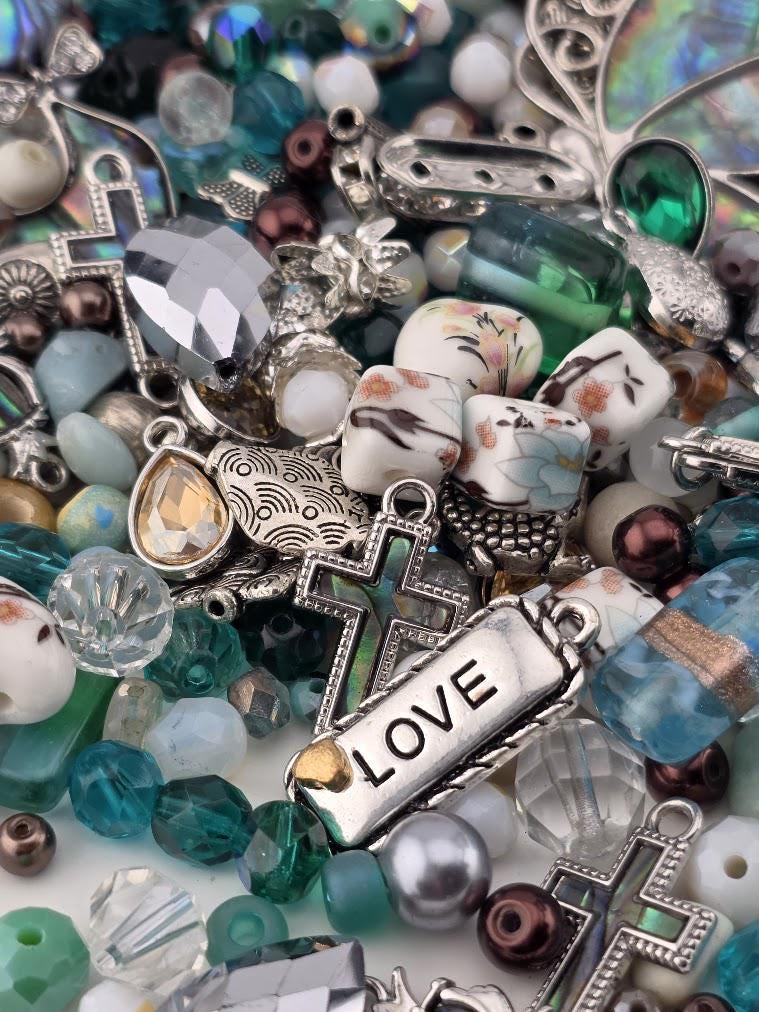 The image is a collection of various beads, charms, and trinkets, including a cross, arranged in a visually appealing manner.