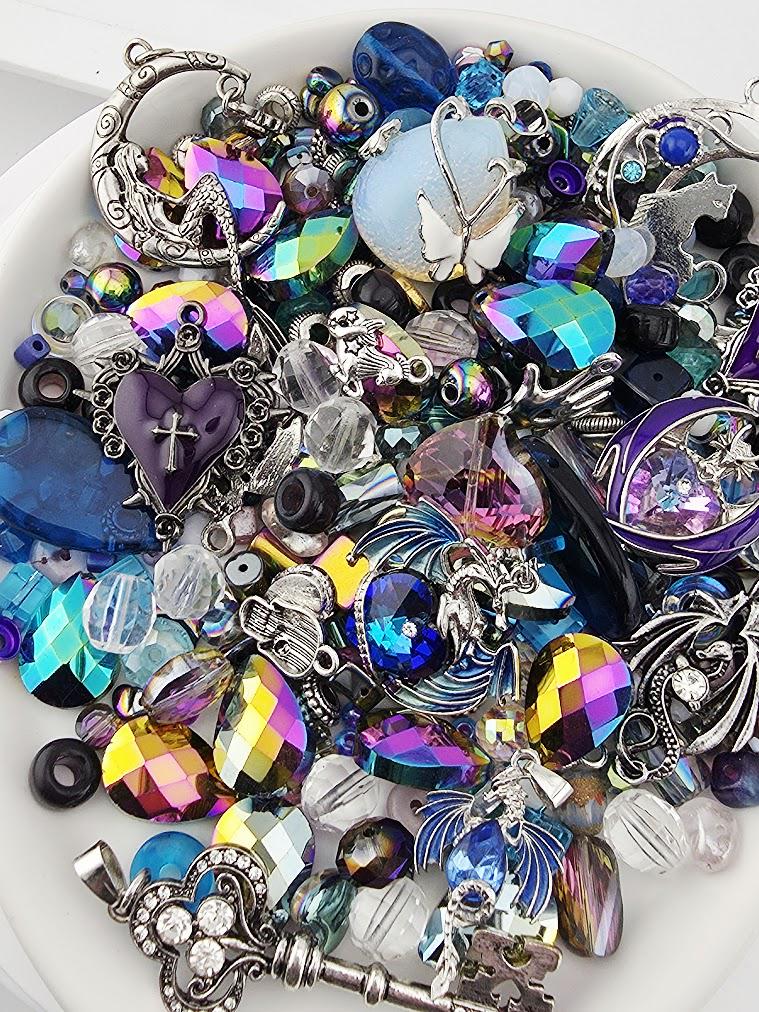 The image is a collection of various colorful beads, charms, and jewelry pieces, including gemstones, pearls, and metalwork, arranged on a white surface.