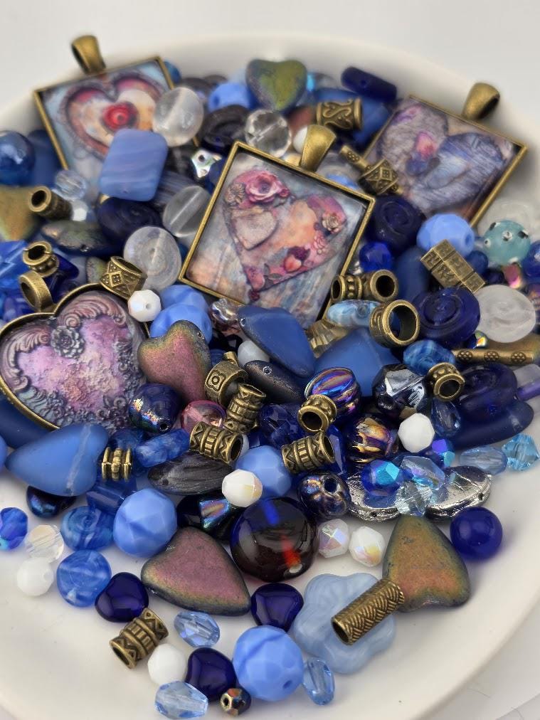 The image is a collection of various beads, charms, and pendants in shades of blue, gold, and purple, arranged on a white surface.