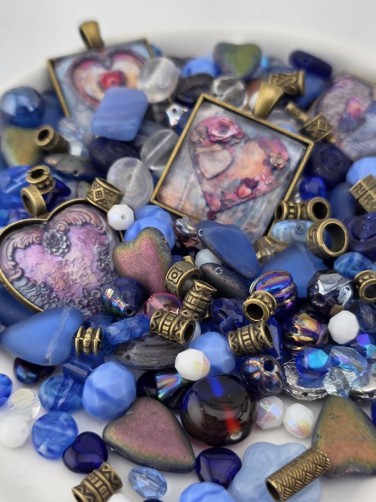 The image is a collection of various colorful beads, charms, and pendants, including heart-shaped and square-shaped pieces, as well as some with intricate designs. The objects are scattered across a surface, creating a visually appealing and diverse arrangement.