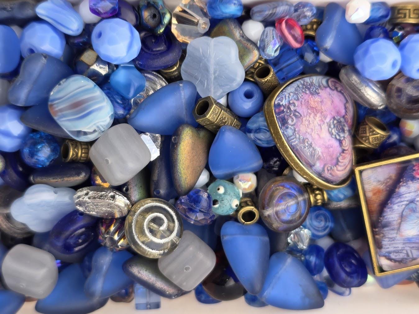 The image is a collection of various blue glass beads, charms, and other glass objects, including some with intricate designs and patterns.