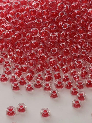 The image is a close-up of numerous red glass beads scattered across a white surface.