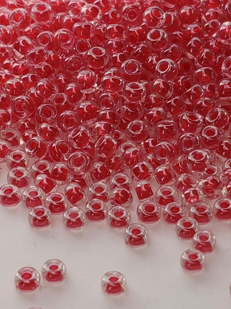 The image is a close-up of numerous red glass beads scattered across a white surface.