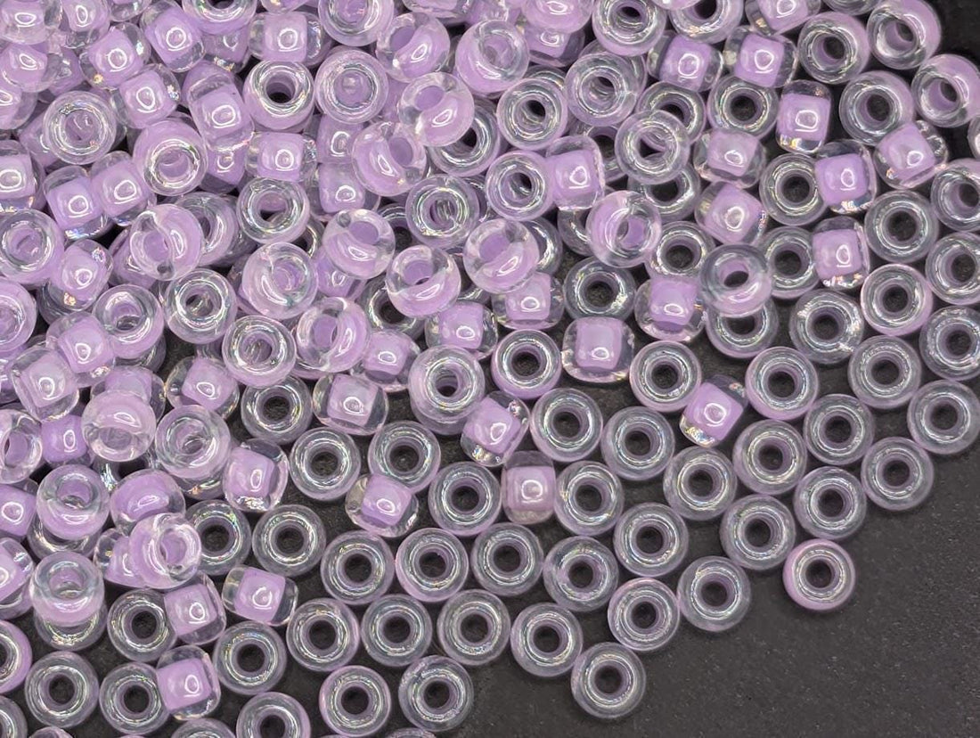 The image is a close-up of numerous clear beads in various shades of purple, scattered across a white surface.