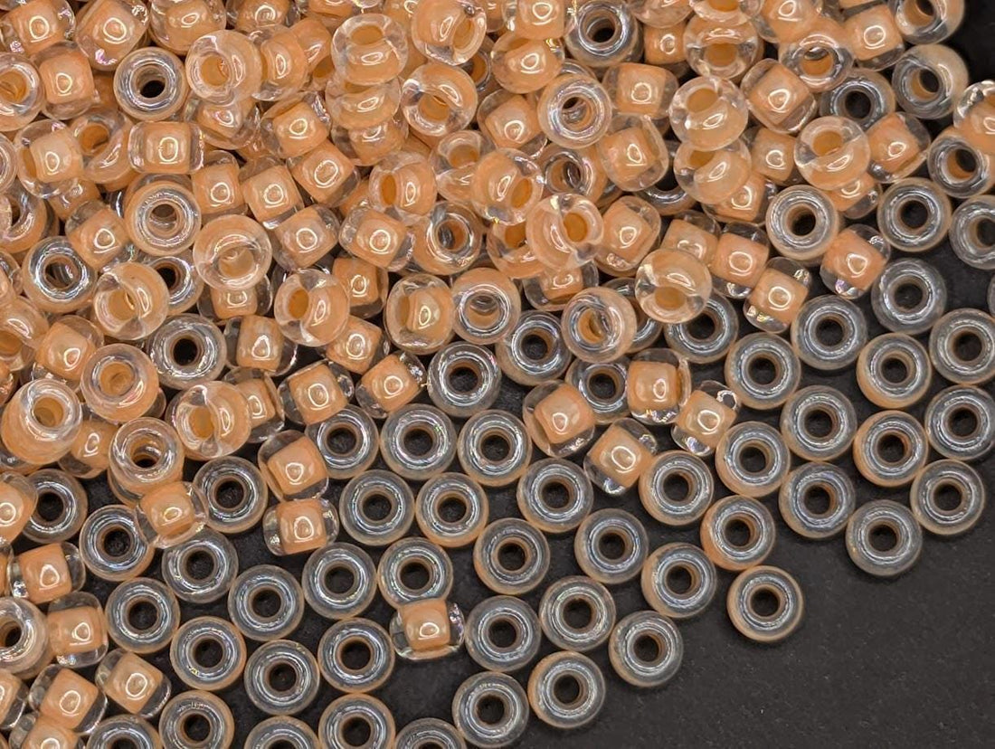 a large pile of clear glass beads in various shades of orange and yellow, scattered across a white surface.
