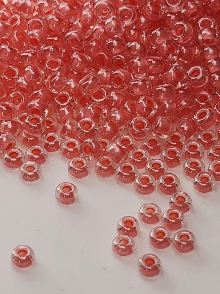 a large pile of small, clear beads in various shades of red, scattered across a white surface.