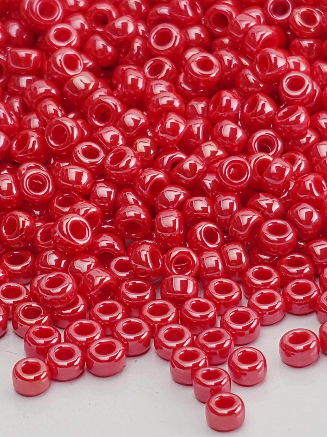 a large pile of red, shiny beads scattered across a white surface.