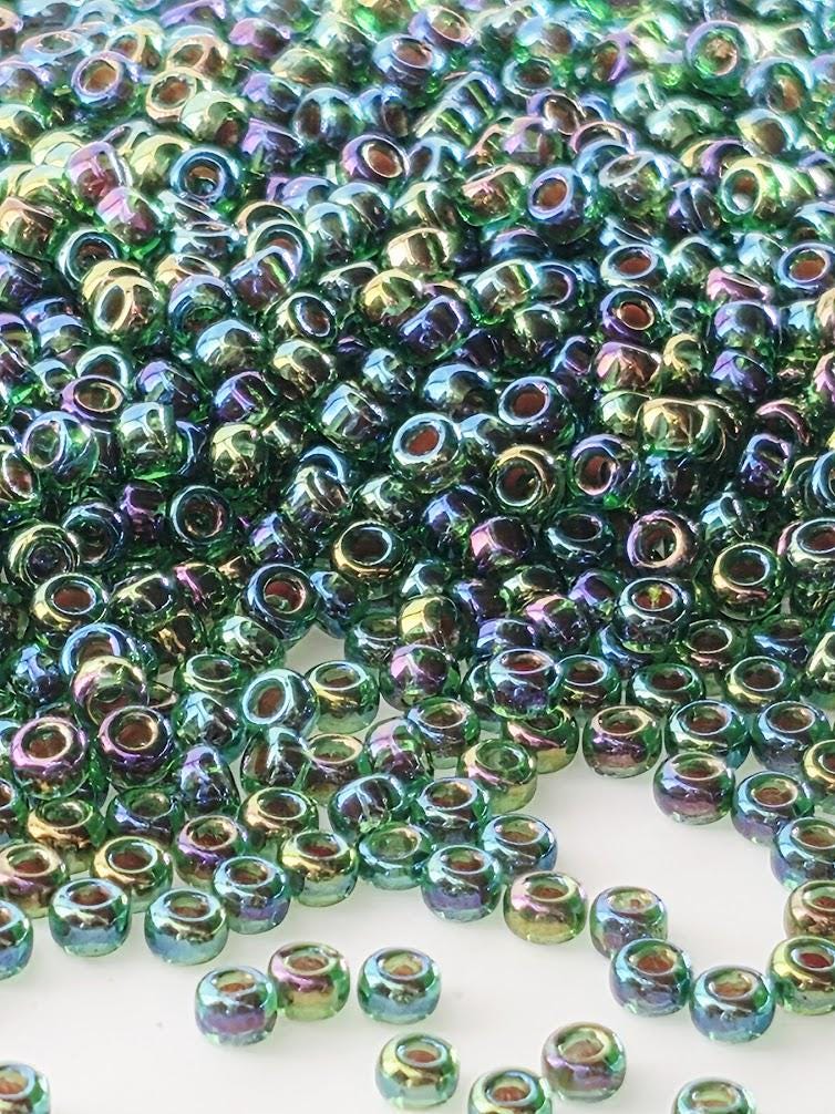 The image is a close-up of numerous multicolored beads, including green, purple, and blue, scattered across a surface.