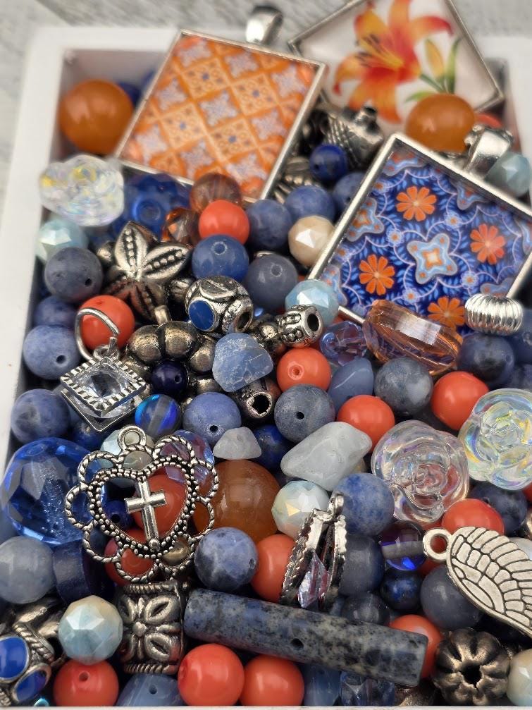 The image is a collection of various beads, charms, and pendants, including blue, orange, and silver elements, arranged in a visually appealing manner.