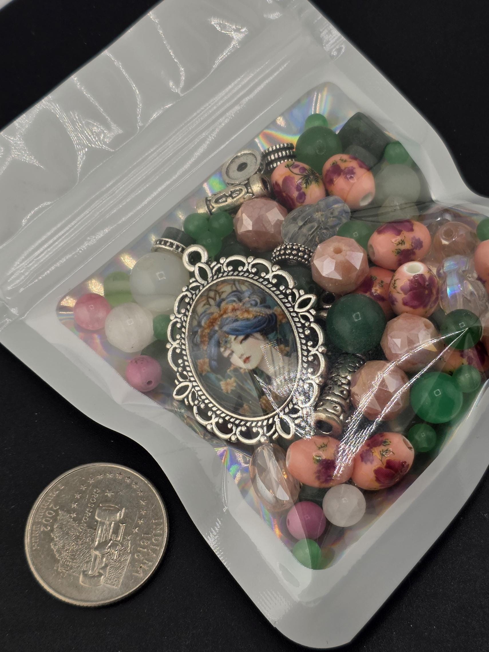 A close-up image of a clear plastic bag filled with various colorful beads, charms, and a silver pendant.