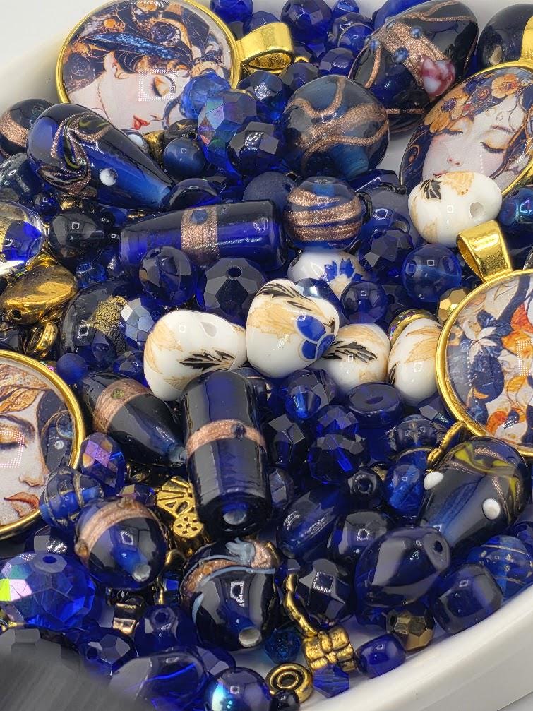 The image is a collection of various blue and gold beads, charms, and glass beads arranged in a bowl or container.