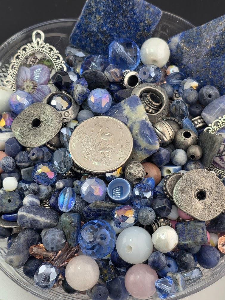 a variety of colorful beads, coins, and other small objects, including blue, white, and silver pieces, arranged in a bowl or container.
