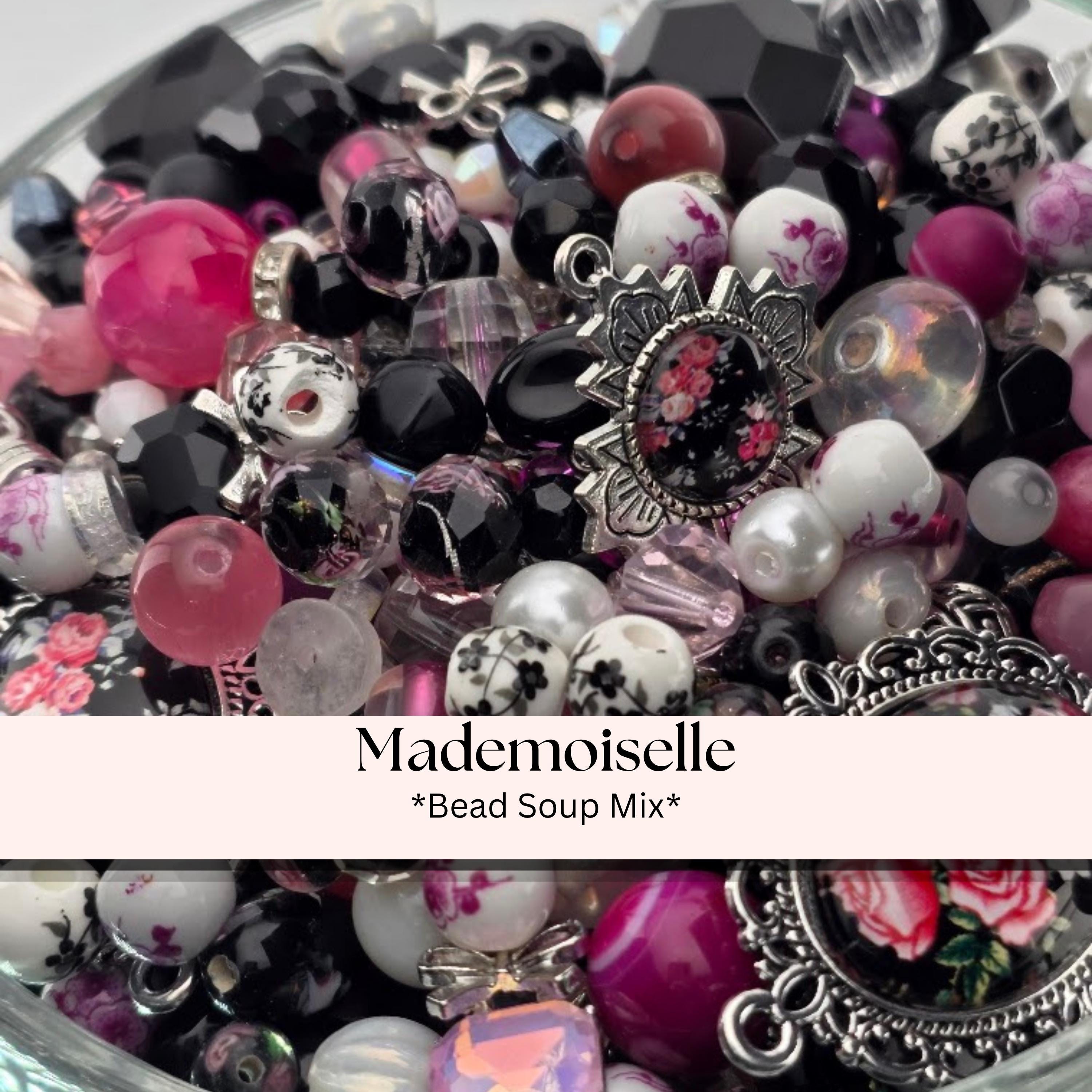 A collection of various beads, charms, and decorative elements, including glass beads, metal charms, and floral-patterned beads, arranged in a bowl or container.