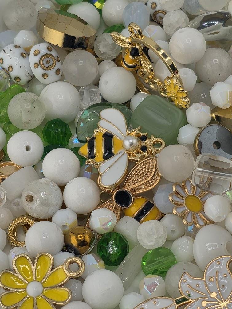 The image is a collage of various beads, charms, and metallic objects, including white, green, yellow, and gold elements.