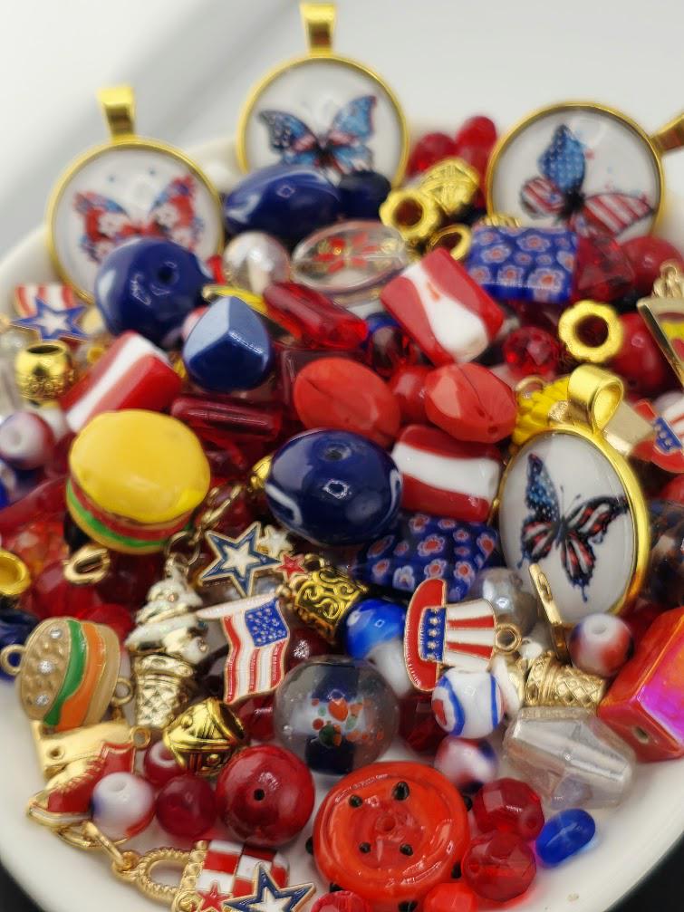 The image is a collection of various colorful beads, buttons, and other decorative items, including some with patriotic designs such as butterflies and stars, arranged on a white surface.