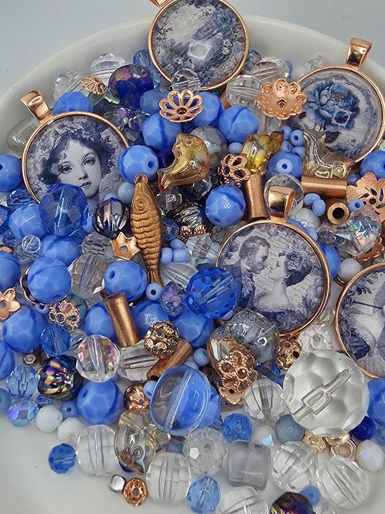 The image is a collection of various beads, charms, and pendants in shades of blue, gold, and clear, arranged in a visually appealing manner.
