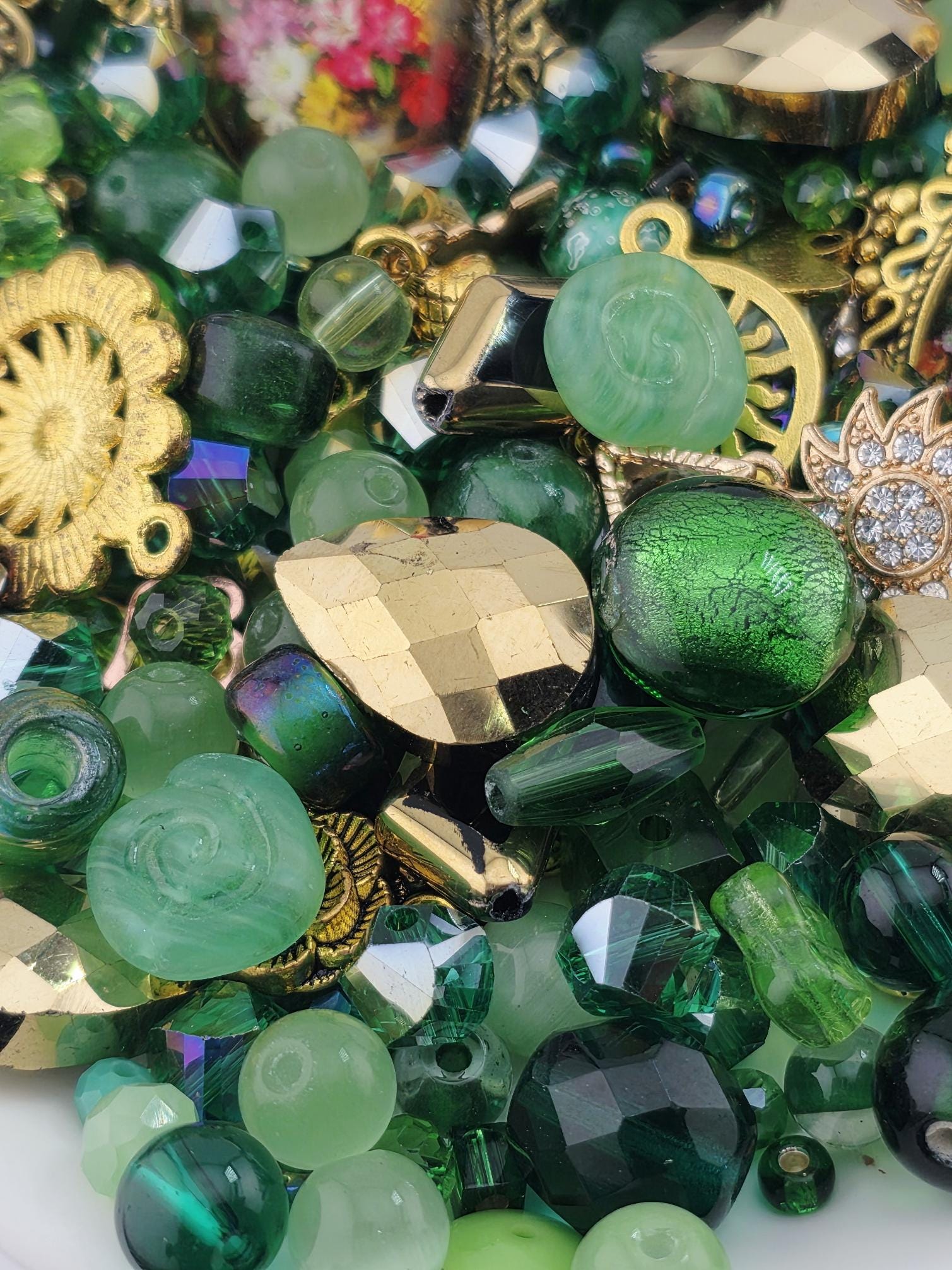 The image is a close-up of a collection of various green glass beads, charms, and other decorative elements.