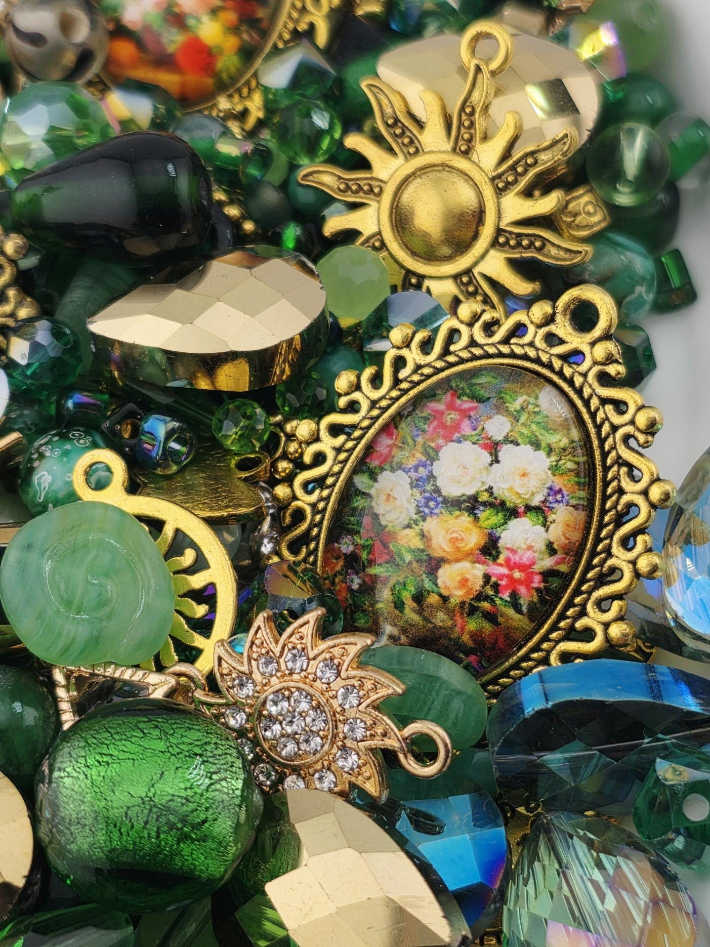 The image is a close-up of a collection of various colorful beads, charms, and other decorative items, including a framed picture of flowers.