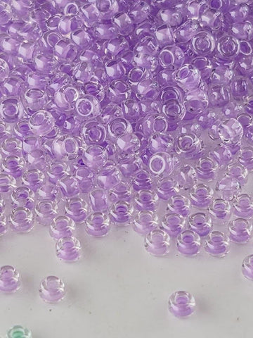 The image is a close-up of numerous clear beads in various shades of purple, scattered across a white surface.