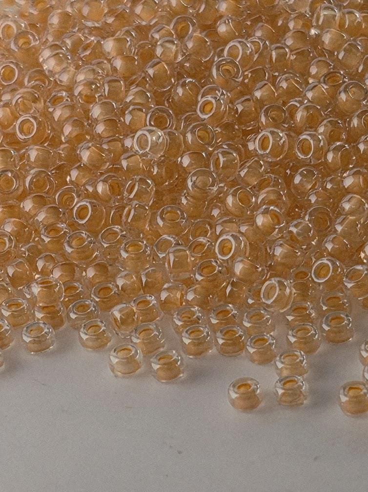 a large pile of clear glass beads in various shades of orange and yellow, scattered across a white surface.