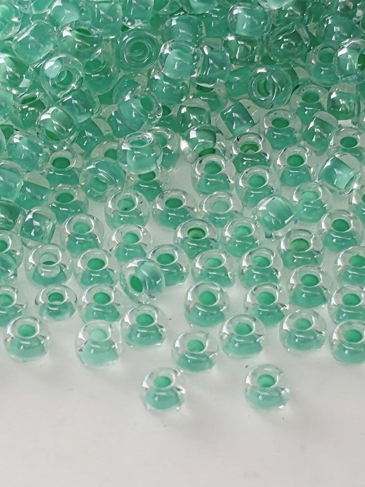 a large number of clear glass beads in various shades of green, scattered across a white background.