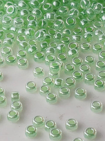 a collection of small, clear glass beads in various shades of green, scattered across a white surface.