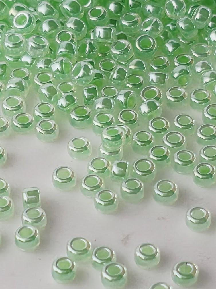 a collection of small, clear glass beads in various shades of green, scattered across a white surface.