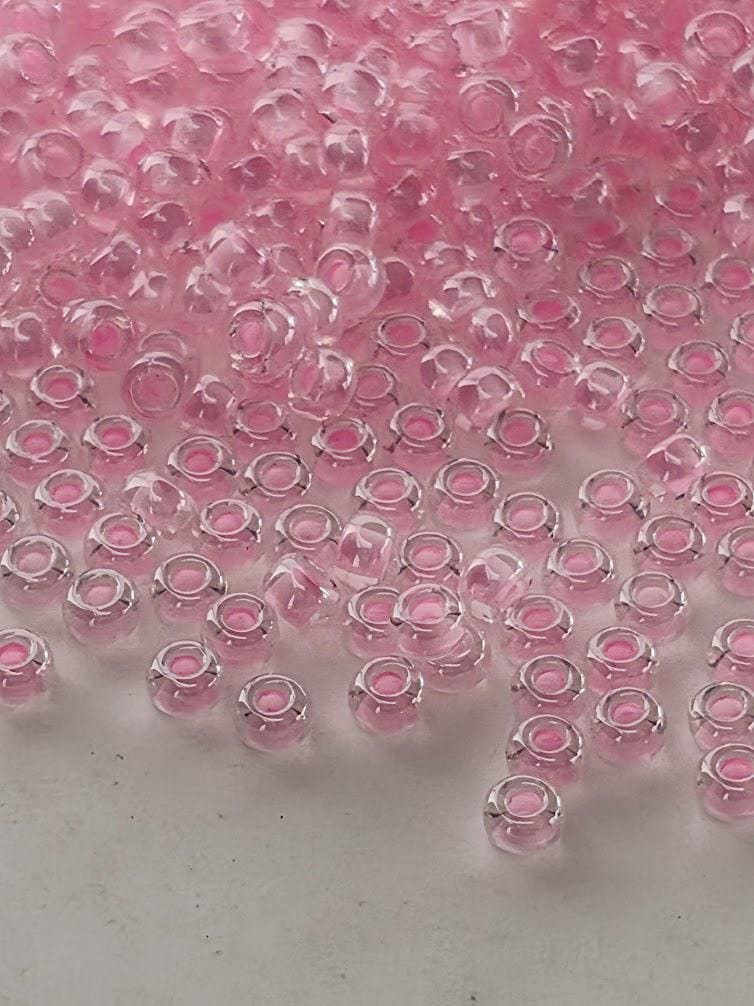 a collection of small, clear glass beads in various shades of pink, scattered across a white surface.