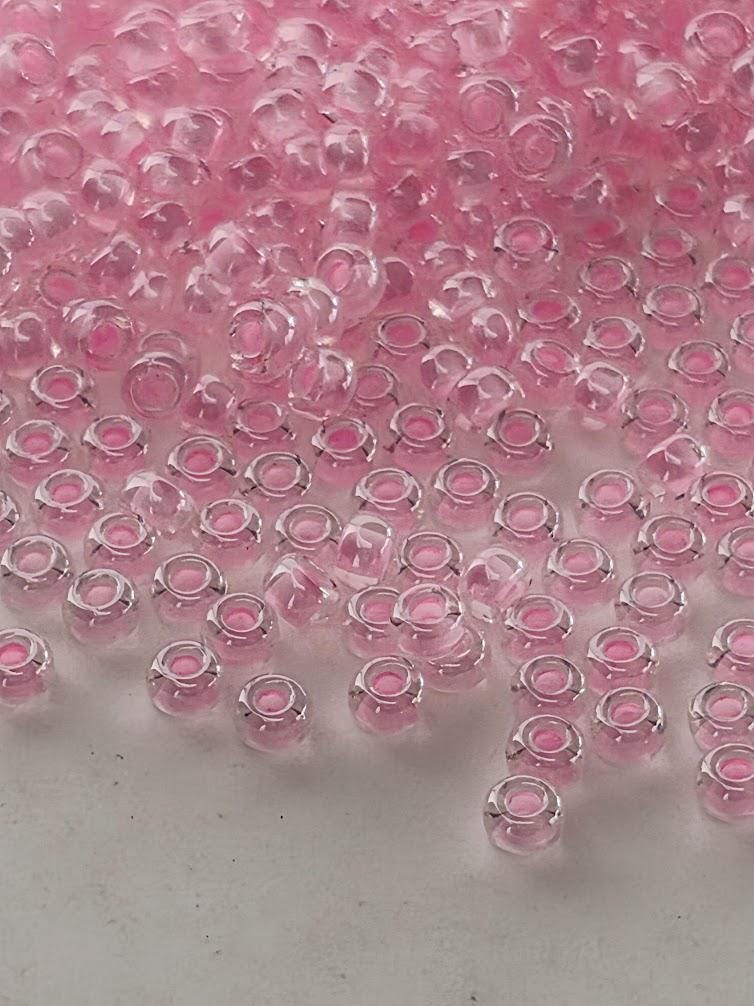 a collection of small, clear glass beads in various shades of pink, scattered across a white surface.
