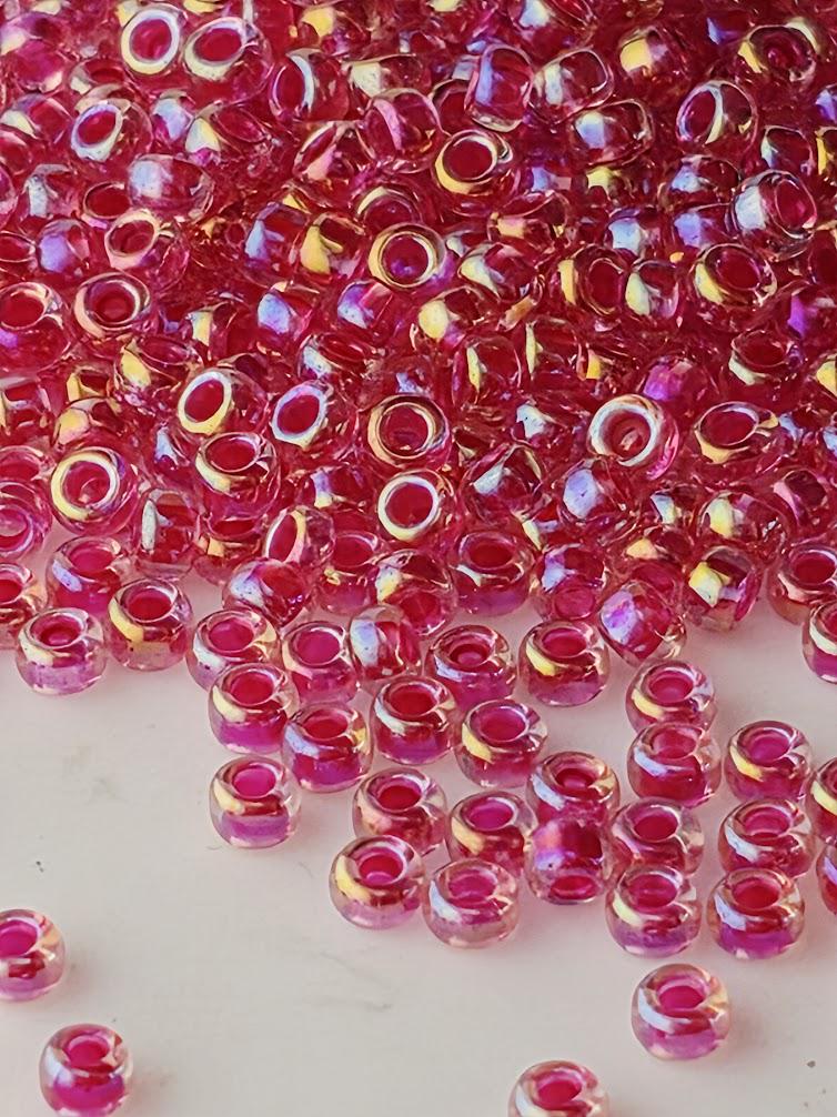 a large pile of small, clear beads in shades of pink and red, scattered across a surface.